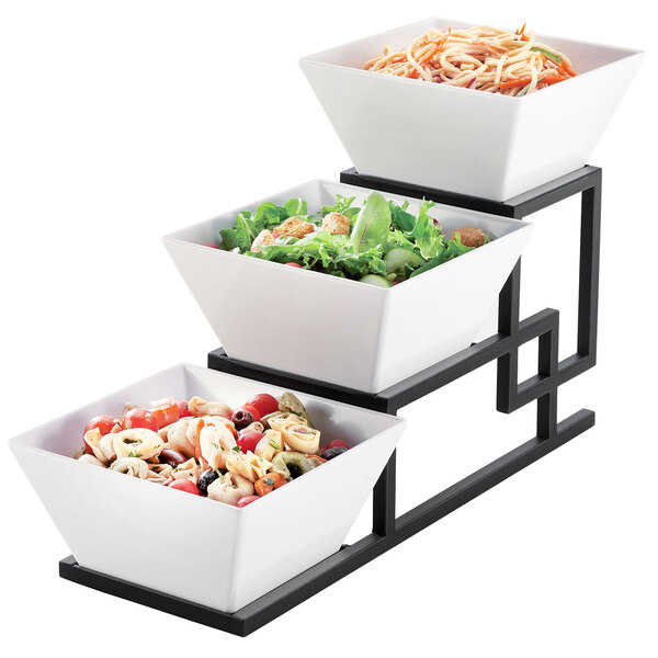 A white square 3 tiered bowl display filled with salads and vegetables.
