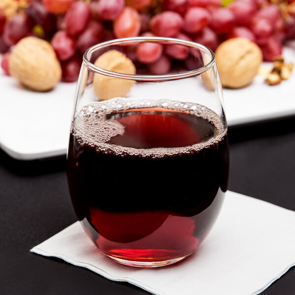 A customizable Arcoroc stemless wine glass filled with red wine on a napkin next to grapes.