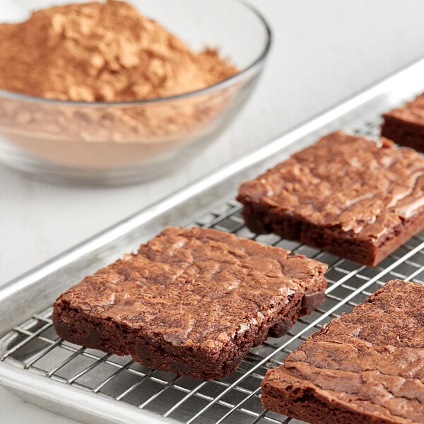 A brownie on a cooling rack with a bowl of HERSHEY'S Natural Cocoa Powder.
