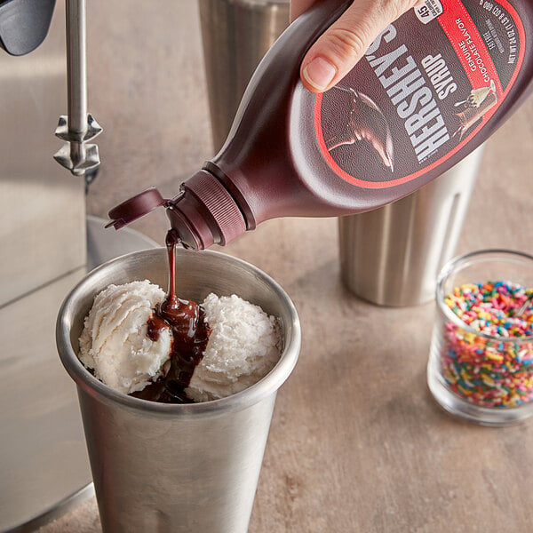 A person pouring HERSHEY'S chocolate syrup onto a scoop of ice cream.