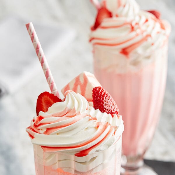 Two strawberry milkshakes topped with whipped cream and strawberries using HERSHEY'S Strawberry Syrup.