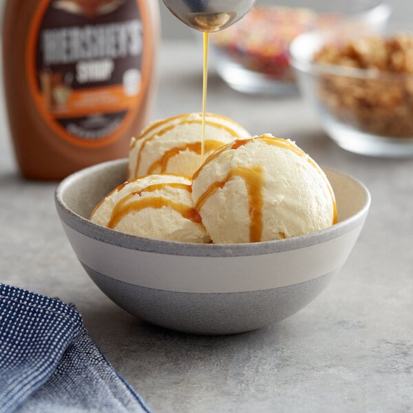 A scoop of ice cream with HERSHEY'S caramel syrup being poured over it.