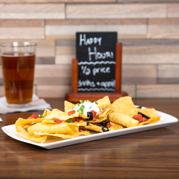 A CAC white china platter with a plate of nachos and a glass of beer on a table.