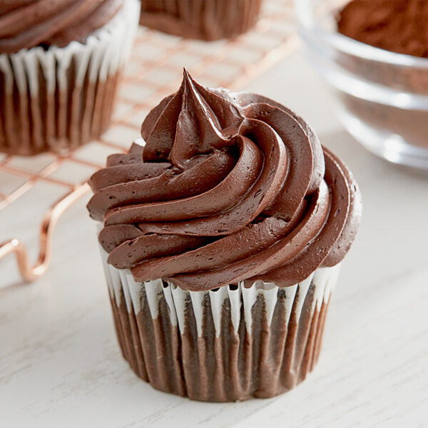 A chocolate cupcake with chocolate frosting next to a bowl of HERSHEY'S Dutch Cocoa Powder.