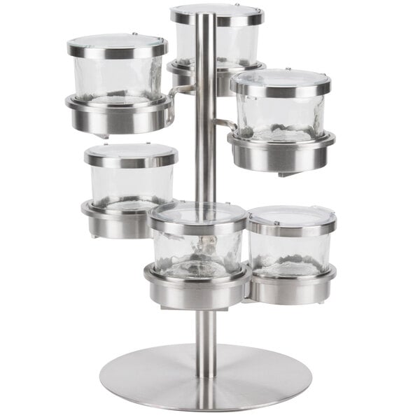 A Cal-Mil stainless steel tiered rotating display with six glass jars on it.