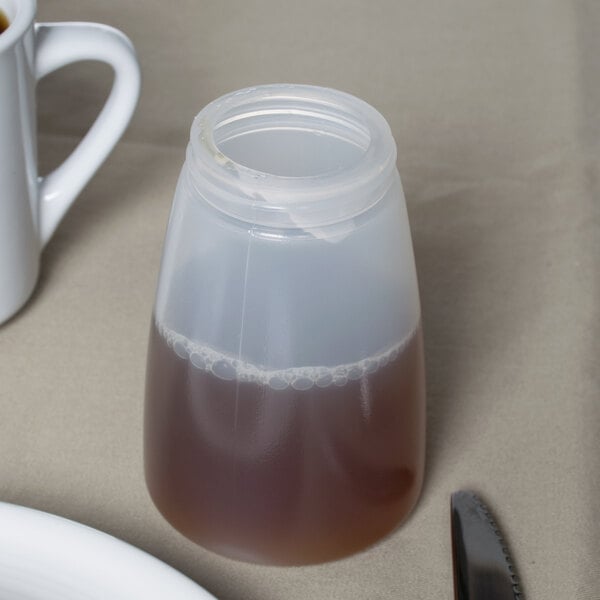 A Tablecraft plastic container with brown liquid in it next to a white mug and a white plate.