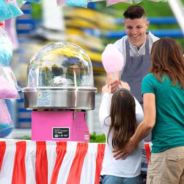 A man using a Carnival King cotton candy machine to make pink cotton candy for a woman holding a child.