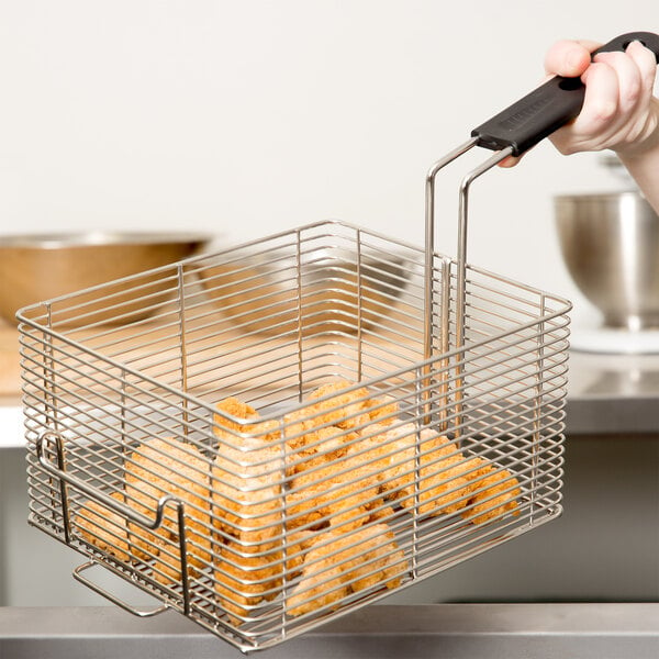 A hand using a Vollrath large fryer basket to cook chicken nuggets.