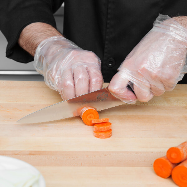 A person in plastic gloves using a Victorinox serrated chef knife to cut carrots.