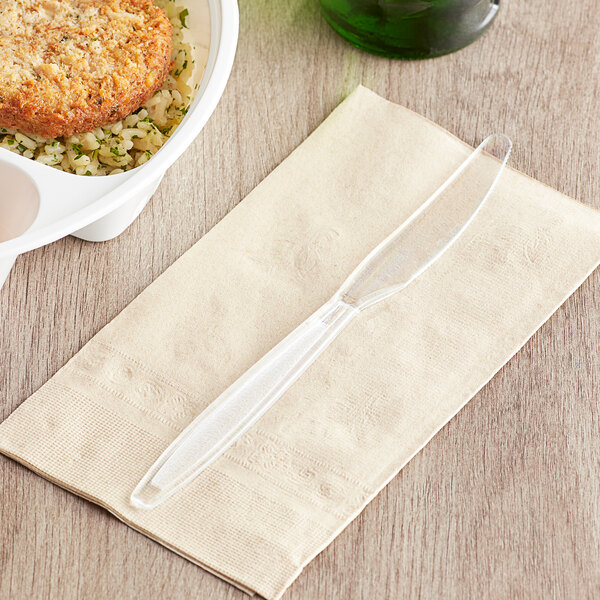 A clear plastic knife on a napkin next to a bowl of food.