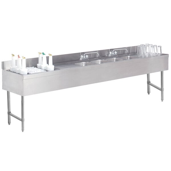 A stainless steel Advance Tabco underbar sink with bottles on it.