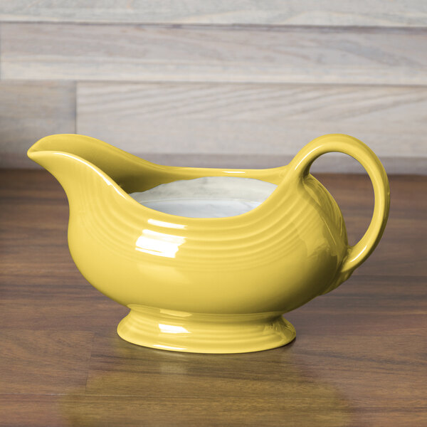 A yellow Fiesta gravy boat with a handle on a wood surface.