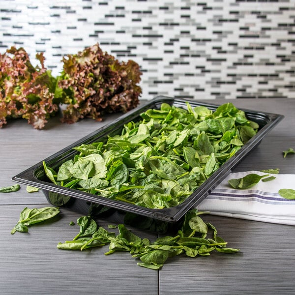 A Carlisle black polycarbonate food pan filled with spinach on a counter.