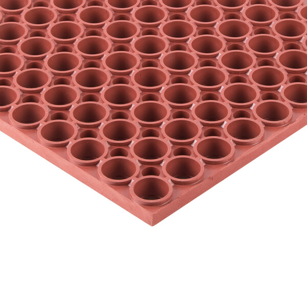 A close up of a large red circular Notrax rubber mat with small holes.