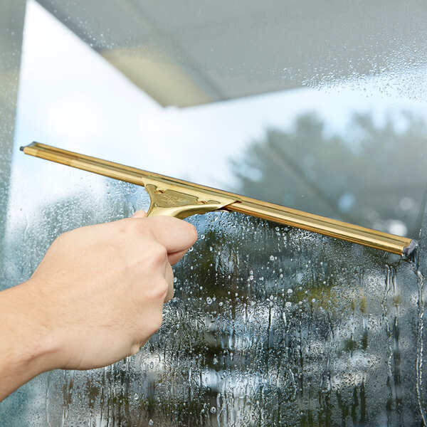 A hand using a Unger brass squeegee to clean a window.