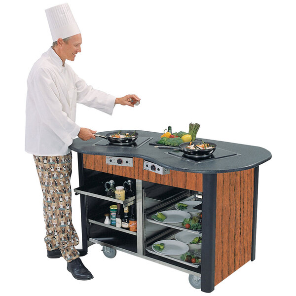A chef standing next to a Lakeside cooking cart with food on a counter in a professional kitchen.