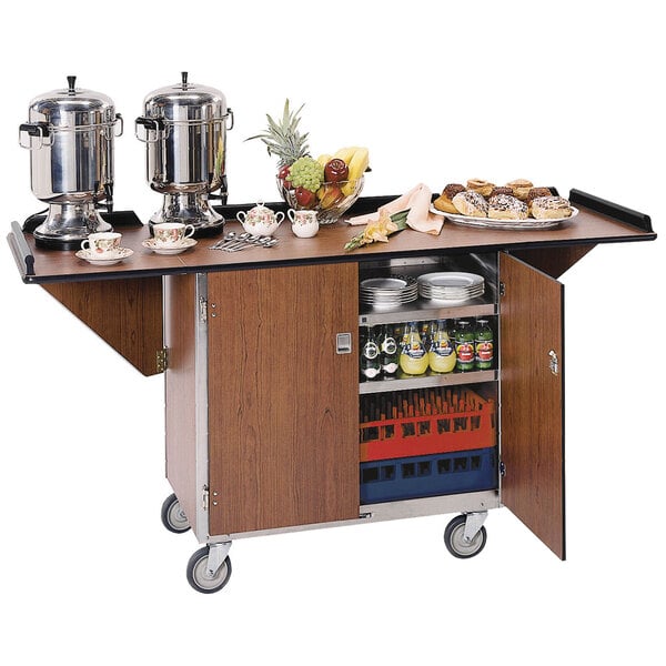 A Lakeside stainless steel beverage service cart with walnut vinyl finish holding food and drinks on a table.