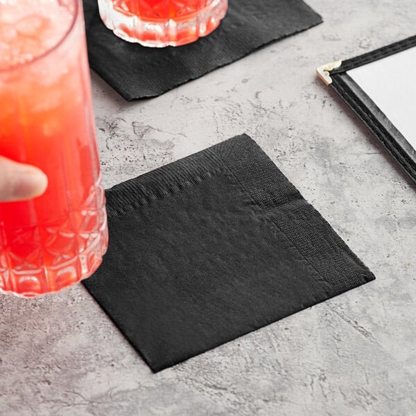 A hand holding a glass with a black Choice Beverage Napkin with a red drink.