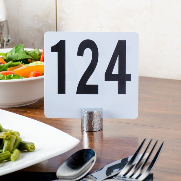 A table with a plate of salad and a table number in an American Metalcraft round hammered aluminum card holder.