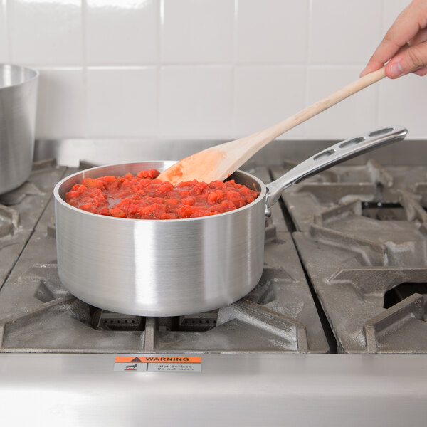 A person stirring red sauce in a Vollrath Wear-Ever sauce pan on a stove with a wooden spoon.
