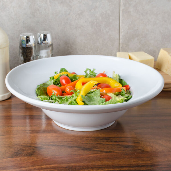 An American Metalcraft round stoneware bowl filled with salad on a table with a glass jar of wine.