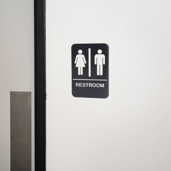 A Thunder Group black and white unisex restroom sign with Braille on a wall.