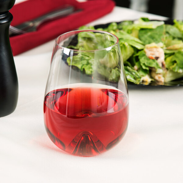 A Stolzle stemless wine glass filled with red wine on a table next to a plate of salad.