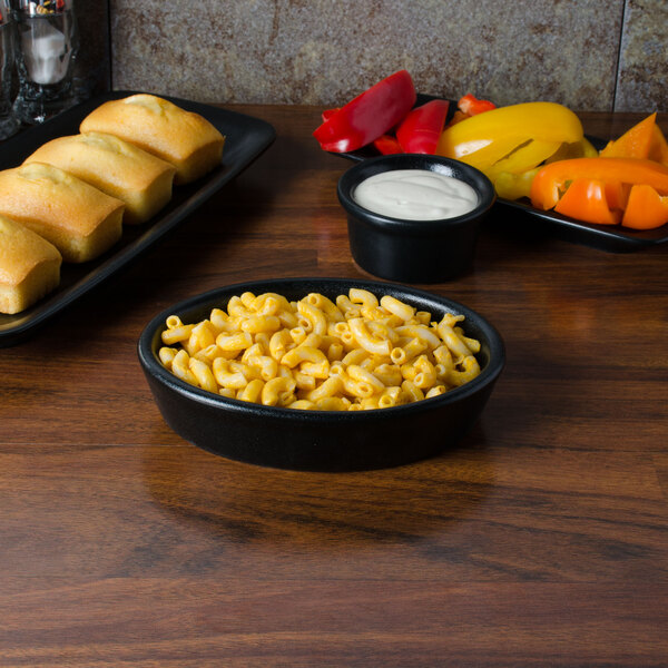 A black oval baker dish filled with macaroni and cheese next to a table of bread and other food.