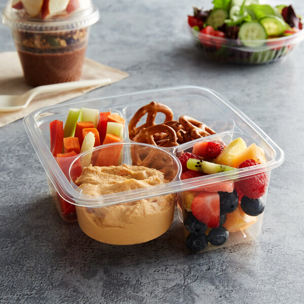 A Fabri-Kal Greenware 3-compartment plastic container with fruit, nuts, and pretzels in it.