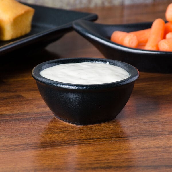 A black Hall China sauce dish filled with carrots and ranch dressing.