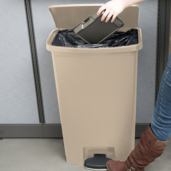 A woman using a black case to put a bag in a Rubbermaid beige Slim Jim trash can.