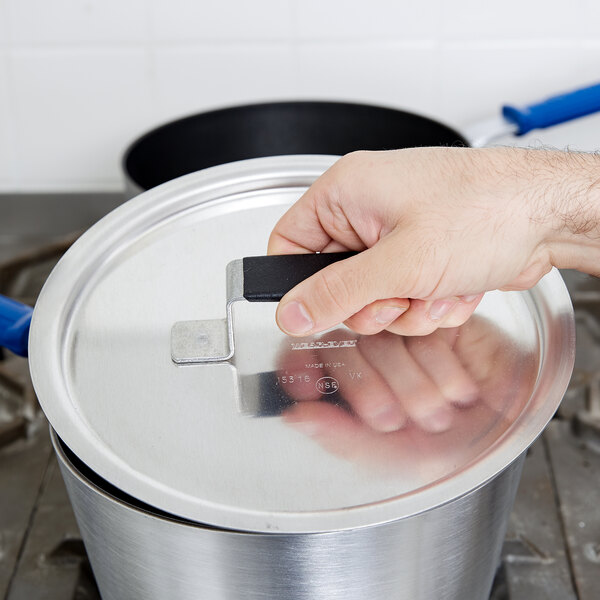 A hand using a Vollrath Wear-Ever aluminum pot lid on a silver pot.