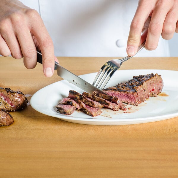 A person using a Victorinox serrated steak knife to cut a piece of meat on a plate.