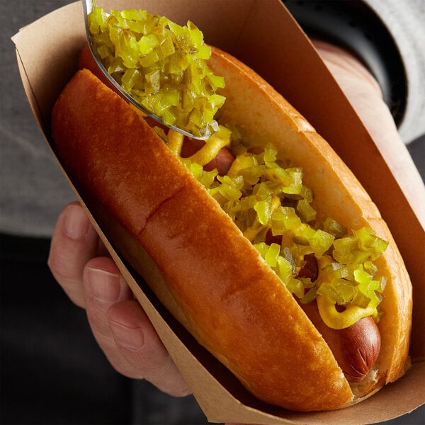 A person holding a hot dog with Del Sol sweet pickle relish and mustard.