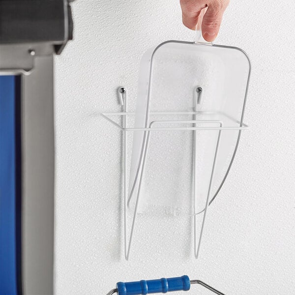 A hand mounts a Choice wall scoop holder to a blue wall.