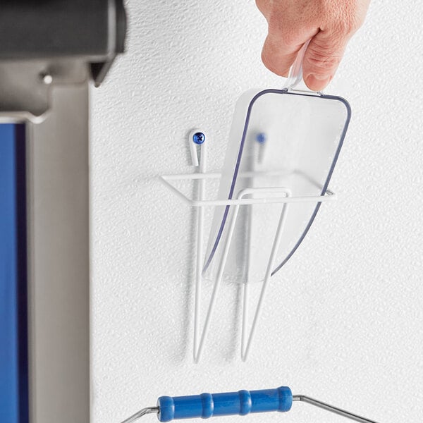 A hand mounts a blue plastic scoop holder on the wall.