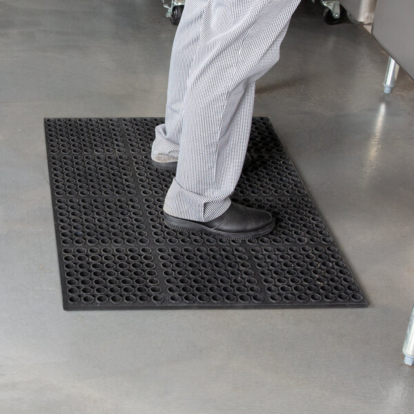 A person standing on a black Cactus Mat VIP Deluxe heavy-duty rubber floor mat.