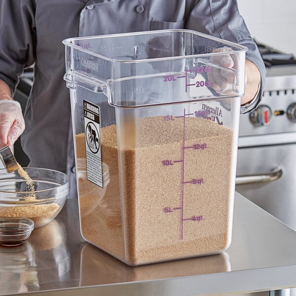 A person using a Cambro square food storage container to pour brown sugar into it.
