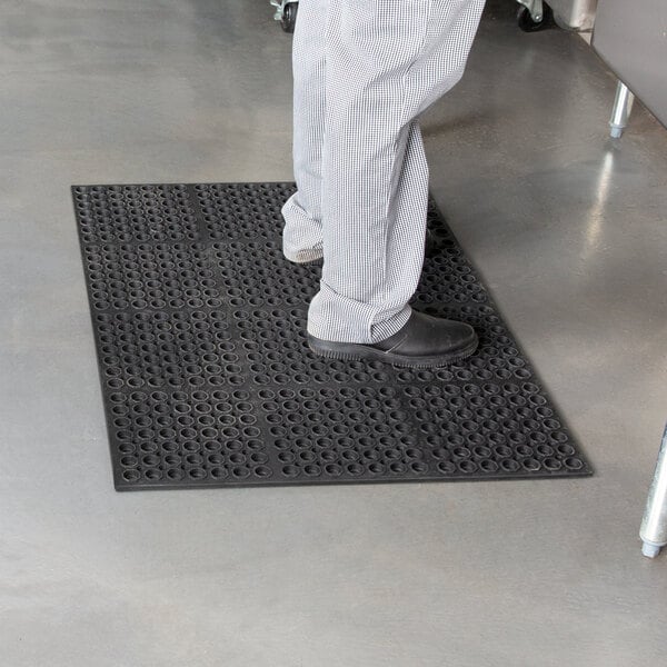 A person standing on a black Cactus Mat anti-fatigue floor mat.