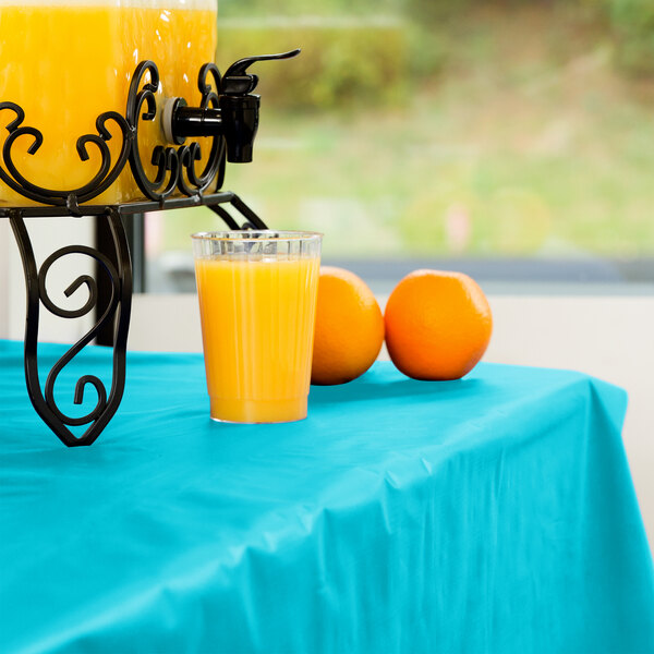 A glass of orange juice on a Bermuda blue disposable table cover next to a drink dispenser.