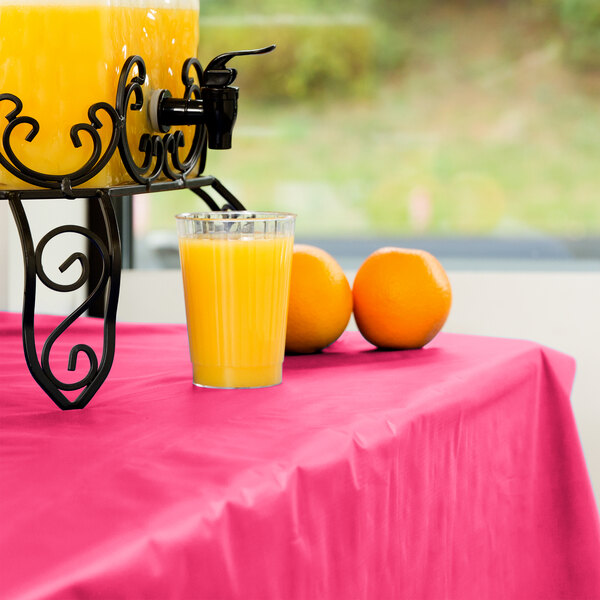 A glass of orange juice on a Creative Converting hot magenta plastic table cover.