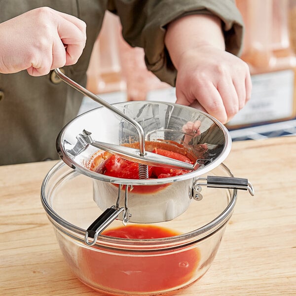 A person using a Tellier stainless steel food mill to make tomato sauce.