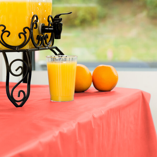 A glass of orange juice sits on a table with a Creative Converting coral orange plastic table cover.