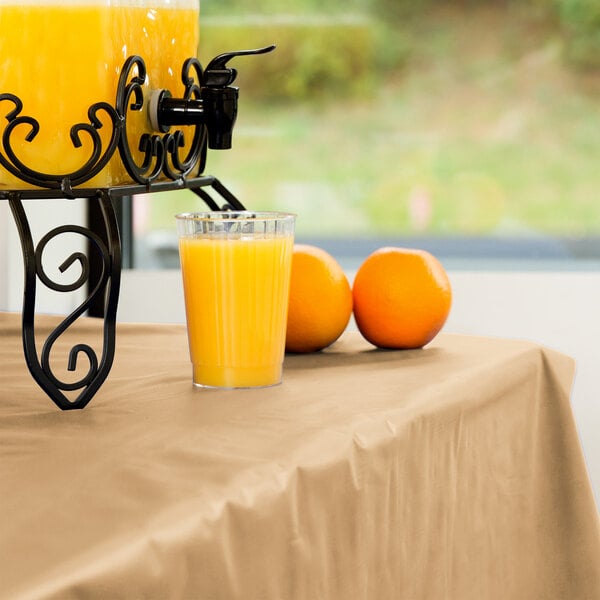 A glass of orange juice on a table with a Creative Converting Glittering Gold plastic table cover.