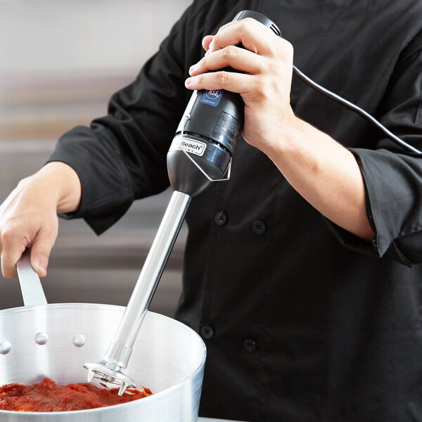 A chef using a Hamilton Beach commercial immersion blender to make sauce.