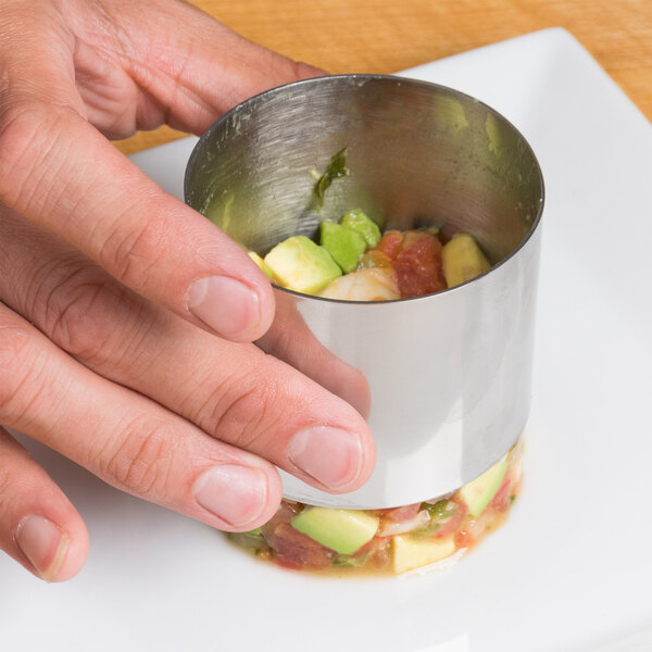 A person holding a stainless steel round cake ring filled with food.