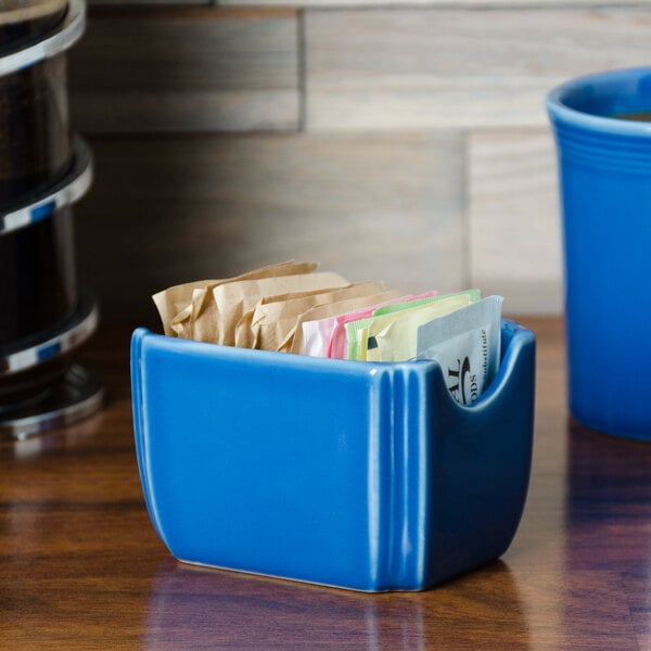 A blue Fiesta sugar caddy on a counter with a packet inside.