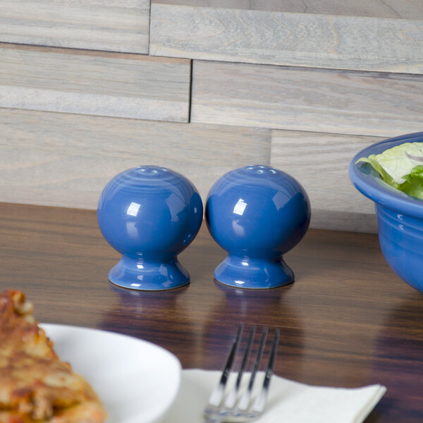 A blue Fiesta pepper shaker on a table with a bowl of salad.