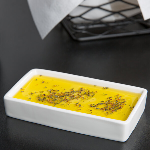 A Tuxton AlumaTux rectangular white china ramekin tray with yellow liquid and spices in it.
