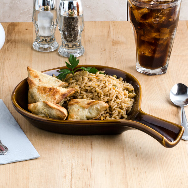 A Tuxton caramel fry pan server filled with rice and chicken on a table with a glass of ice water.